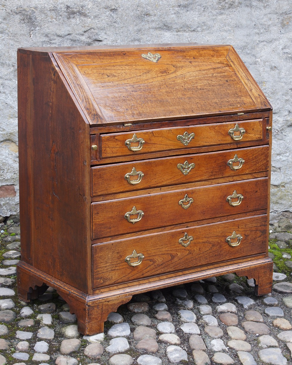 An early eighteenth-century elm slant-front bureau featuring four graduated drawers with brass drop handles and bracket feet. View II