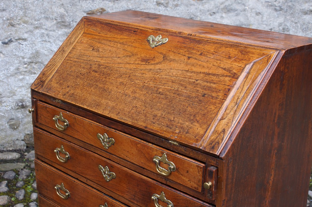 An early eighteenth-century elm slant-front bureau featuring four graduated drawers with brass drop handles and bracket feet. View IV
