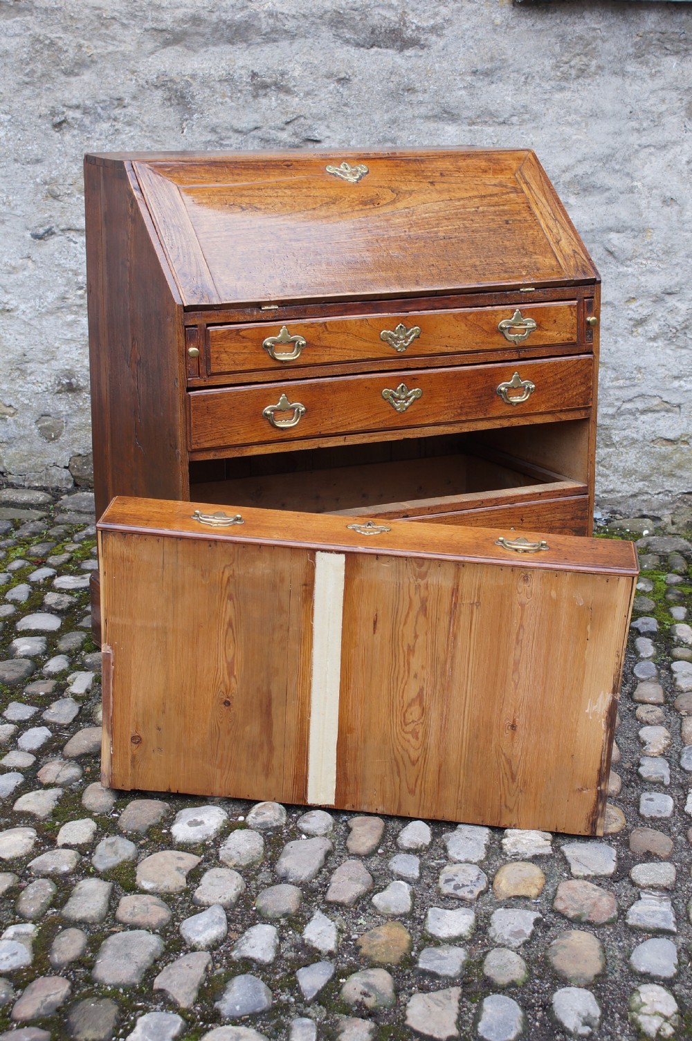 An early eighteenth-century elm slant-front bureau featuring four graduated drawers with brass drop handles and bracket feet. View VI