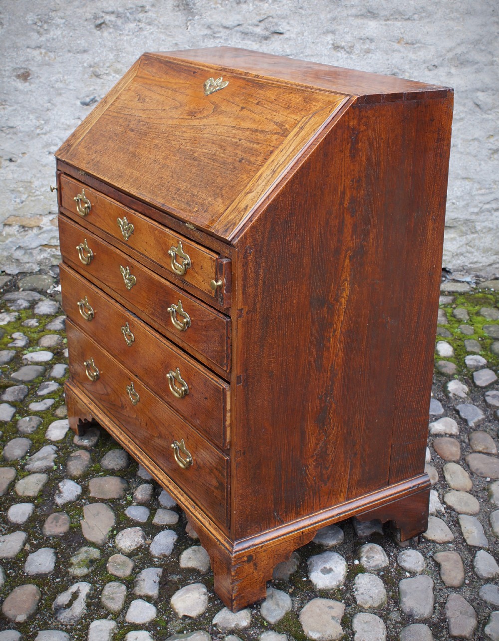 An early eighteenth-century elm slant-front bureau featuring four graduated drawers with brass drop handles and bracket feet. View VIII