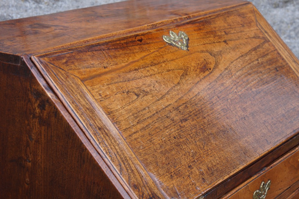 An early eighteenth-century elm slant-front bureau featuring four graduated drawers with brass drop handles and bracket feet. View IX