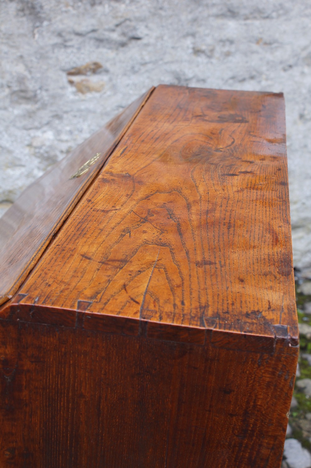 An early eighteenth-century elm slant-front bureau featuring four graduated drawers with brass drop handles and bracket feet. View XI
