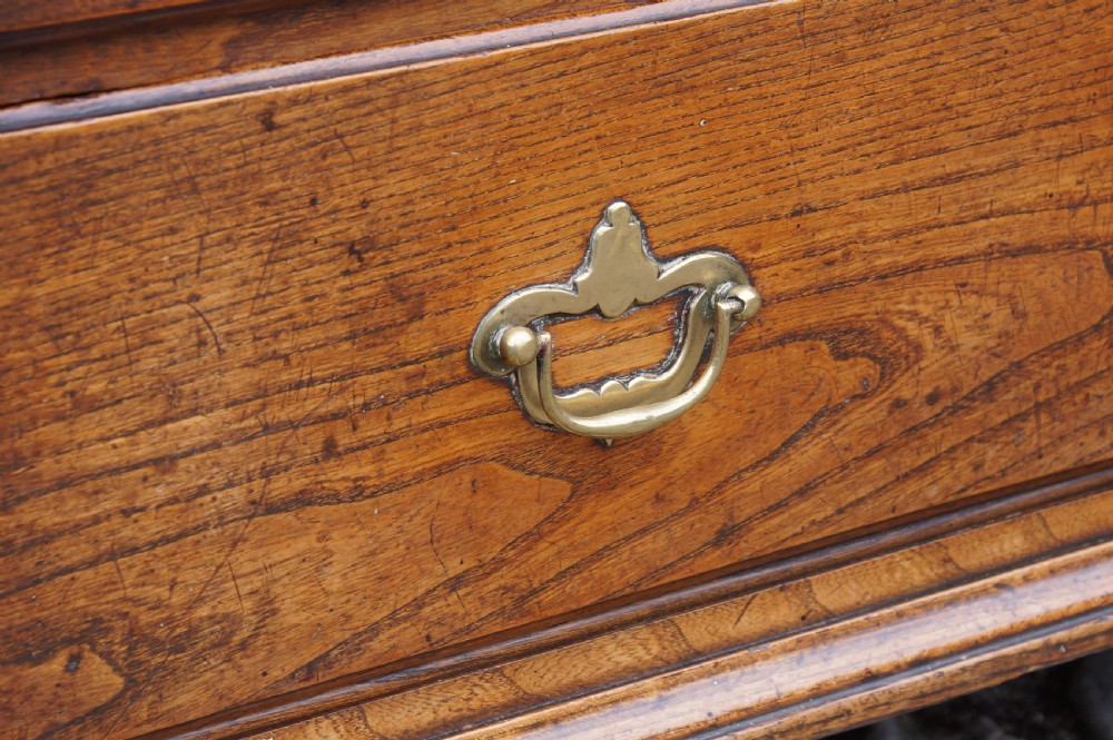An early eighteenth-century elm slant-front bureau featuring four graduated drawers with brass drop handles and bracket feet. View XIII