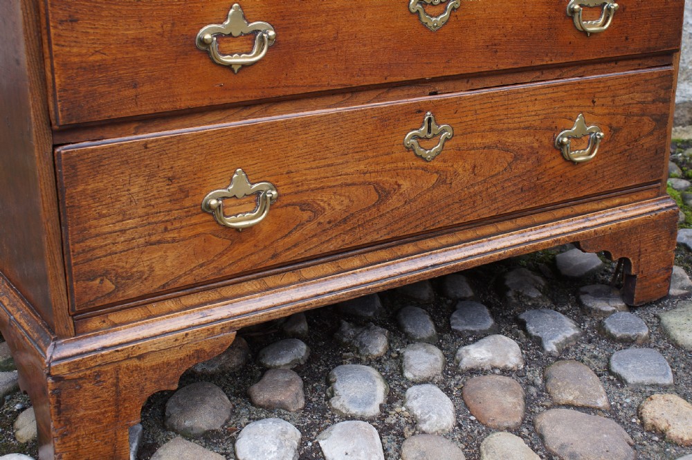 An early eighteenth-century elm slant-front bureau featuring four graduated drawers with brass drop handles and bracket feet. View XIV