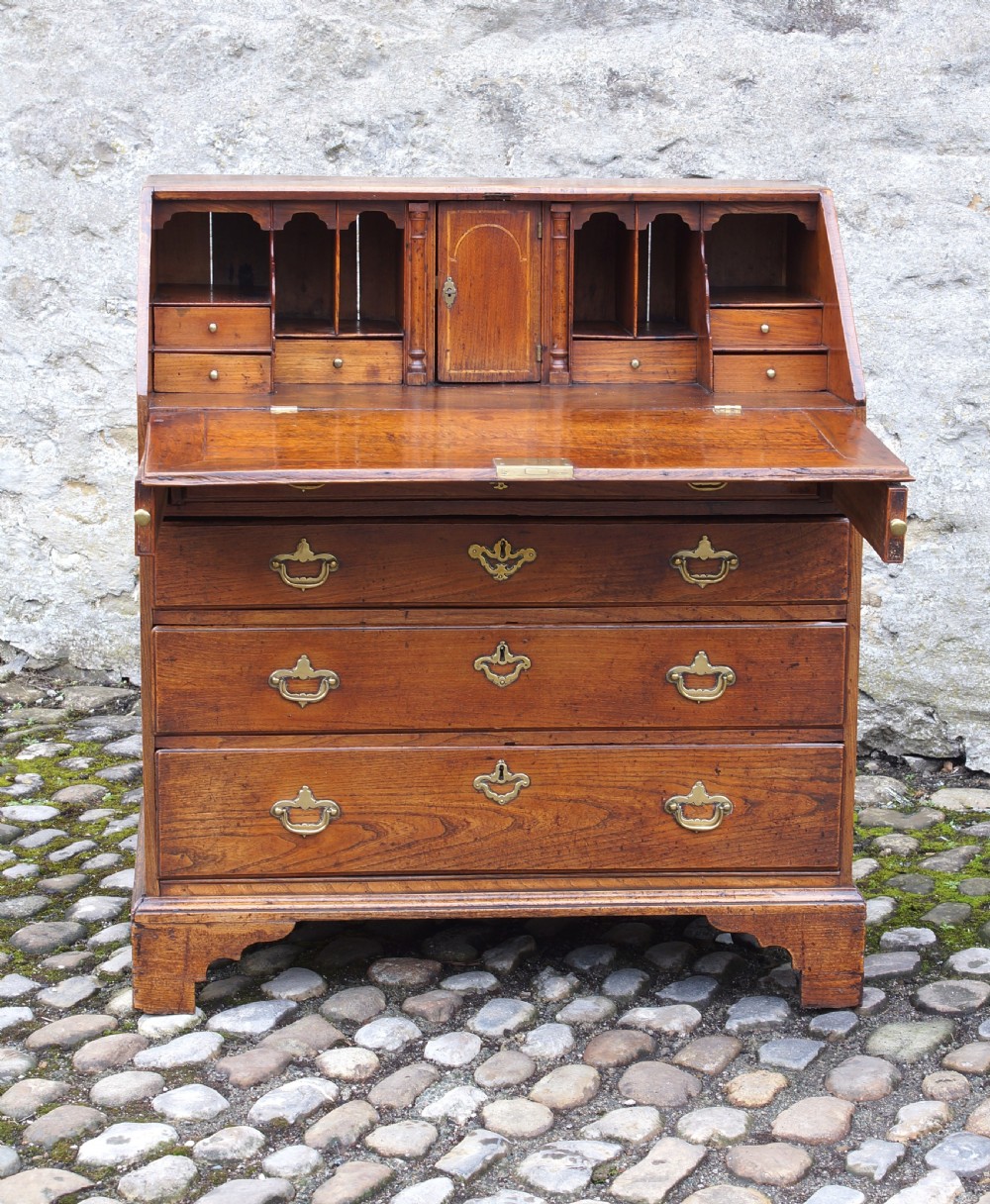 An early eighteenth-century elm slant-front bureau featuring four graduated drawers with brass drop handles and bracket feet. View XVI