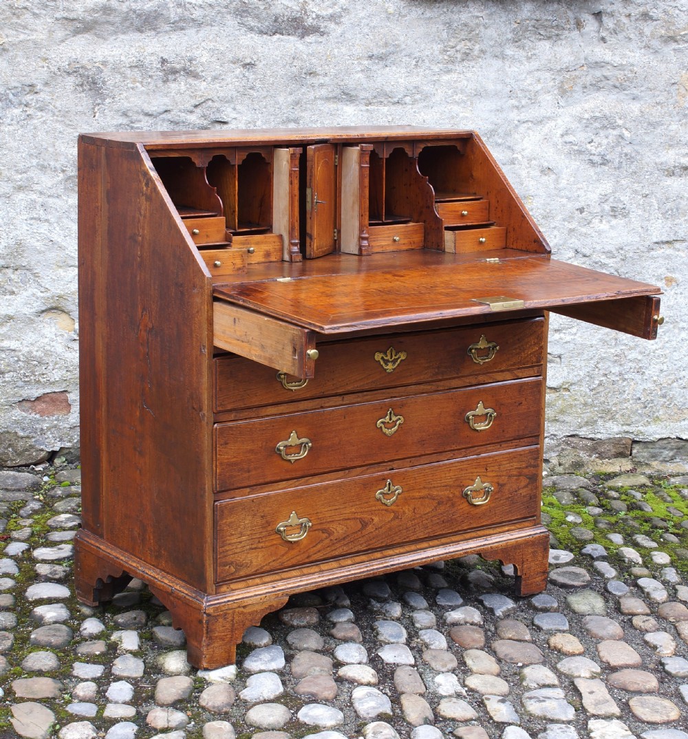 An early eighteenth-century elm slant-front bureau featuring four graduated drawers with brass drop handles and bracket feet. View XVII
