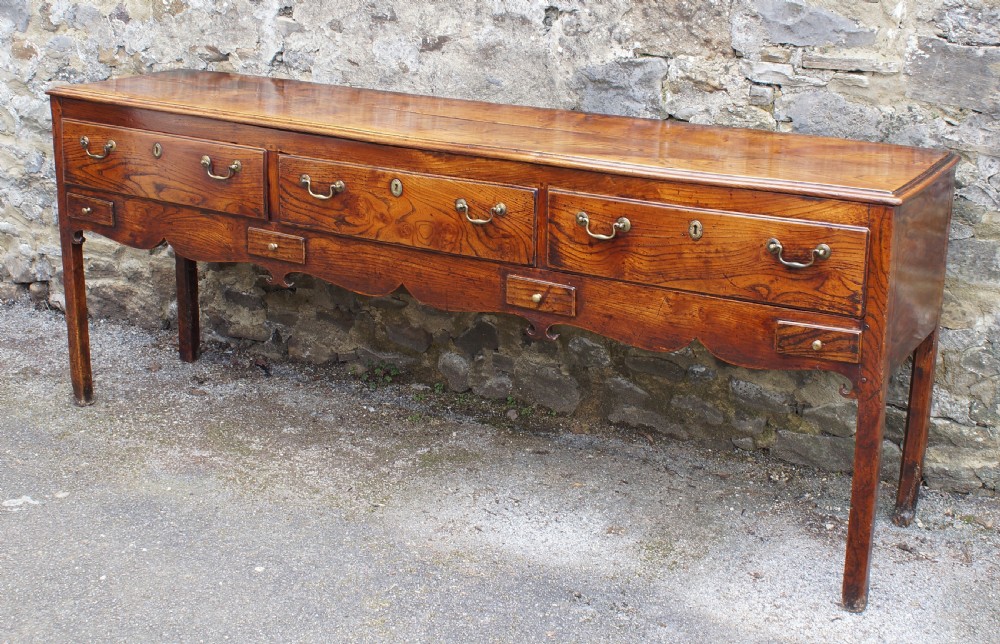 An eighteenth-century warm brown elm dresser base featuring three primary drawers with brass handles above four small drawers set into a scalloped apron. View IV