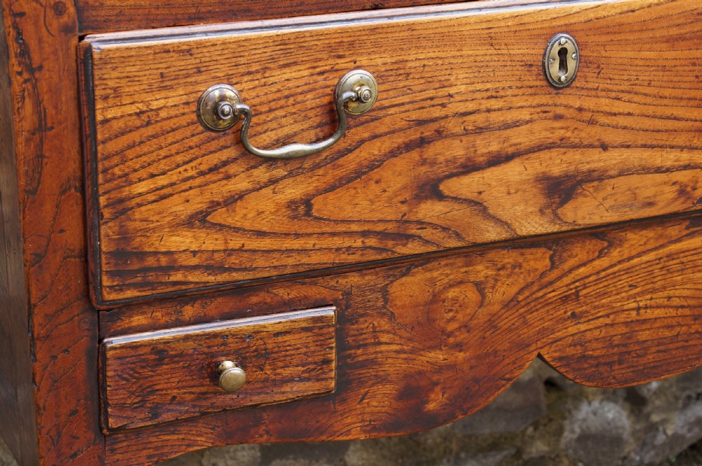 An eighteenth-century warm brown elm dresser base featuring three primary drawers with brass handles above four small drawers set into a scalloped apron. View VI