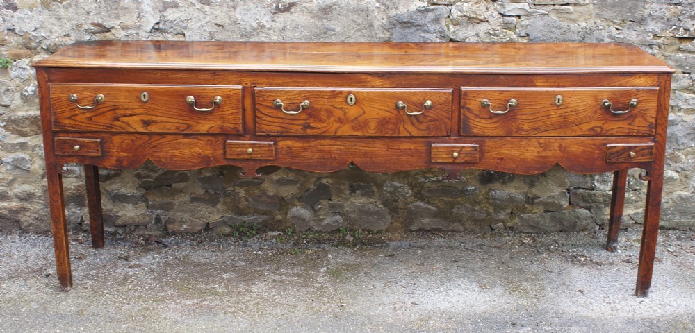 An eighteenth-century warm brown elm dresser base featuring three primary drawers with brass handles above four small drawers set into a scalloped apron. View VIII