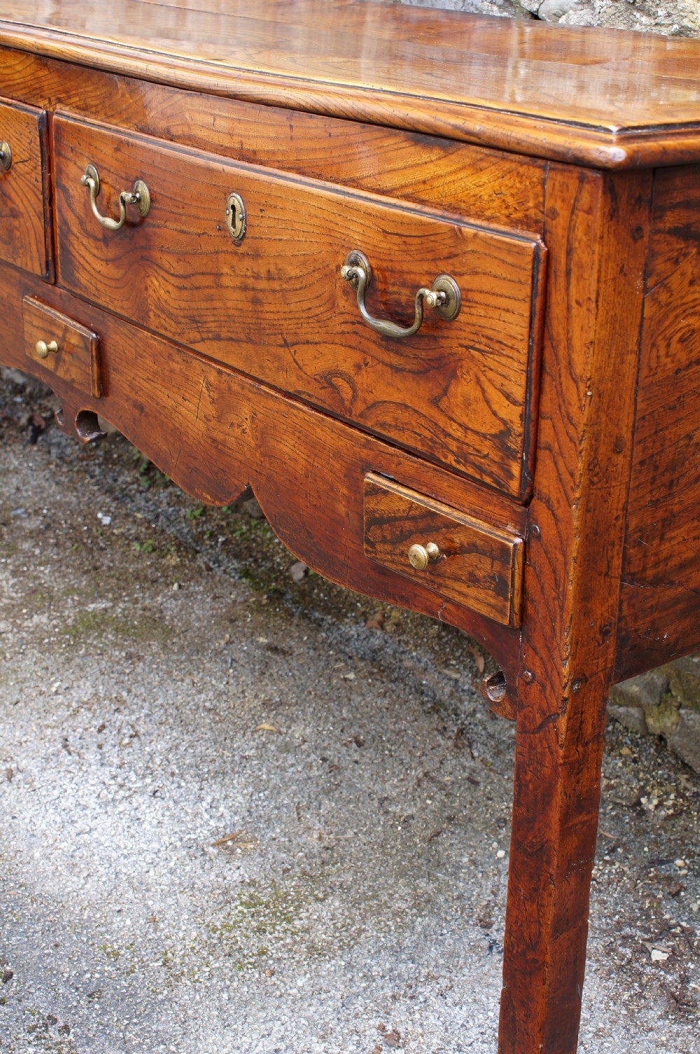 An eighteenth-century warm brown elm dresser base featuring three primary drawers with brass handles above four small drawers set into a scalloped apron. View XII