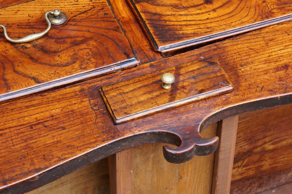 An eighteenth-century warm brown elm dresser base featuring three primary drawers with brass handles above four small drawers set into a scalloped apron. View XX