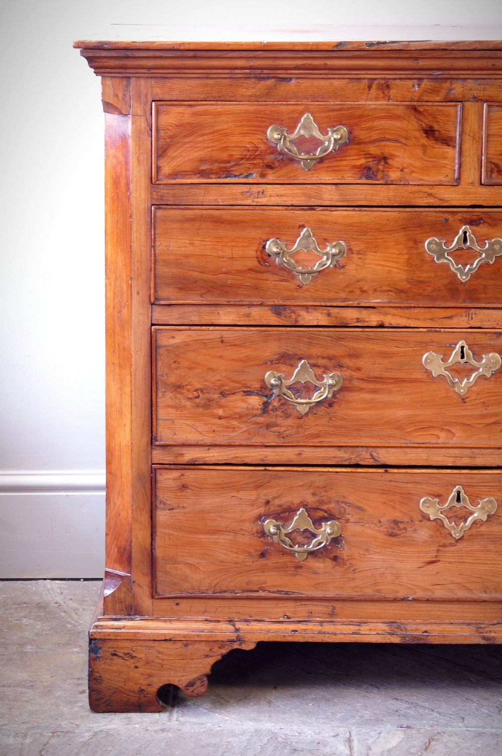An 18th-century Georgian chest of drawers crafted from highly figured warm honey-toned yew wood with two short drawers over three long drawers and brass batwing handles. View IV