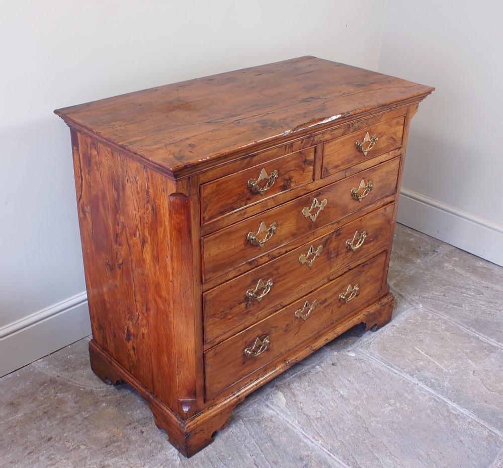 An 18th-century Georgian chest of drawers crafted from highly figured warm honey-toned yew wood with two short drawers over three long drawers and brass batwing handles. View V