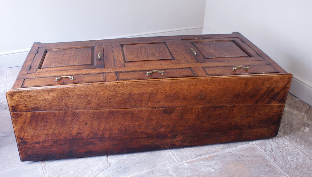 A Georgian oak dresser base featuring three top drawers with brass handles above three panelled cupboard doors. View II