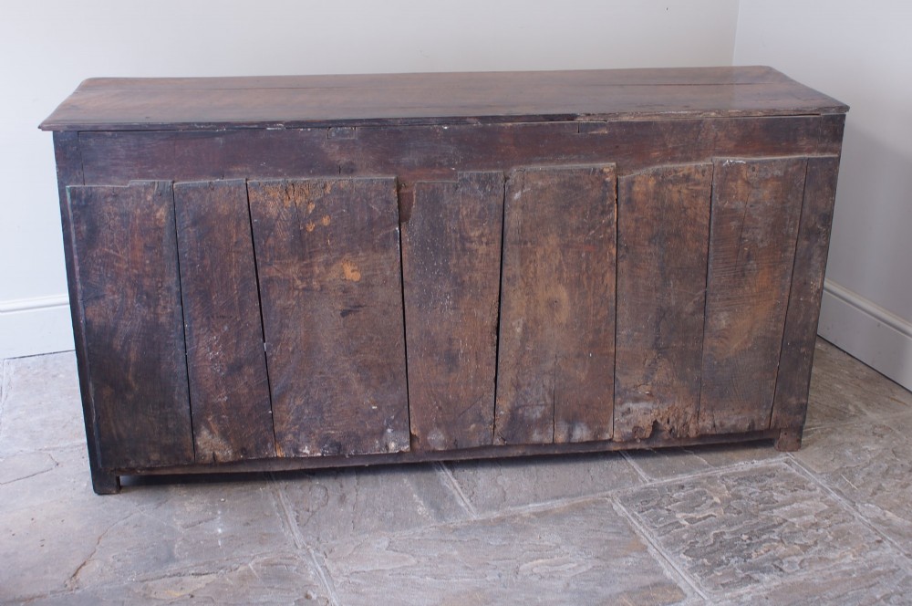 A Georgian oak dresser base featuring three top drawers with brass handles above three panelled cupboard doors. View V