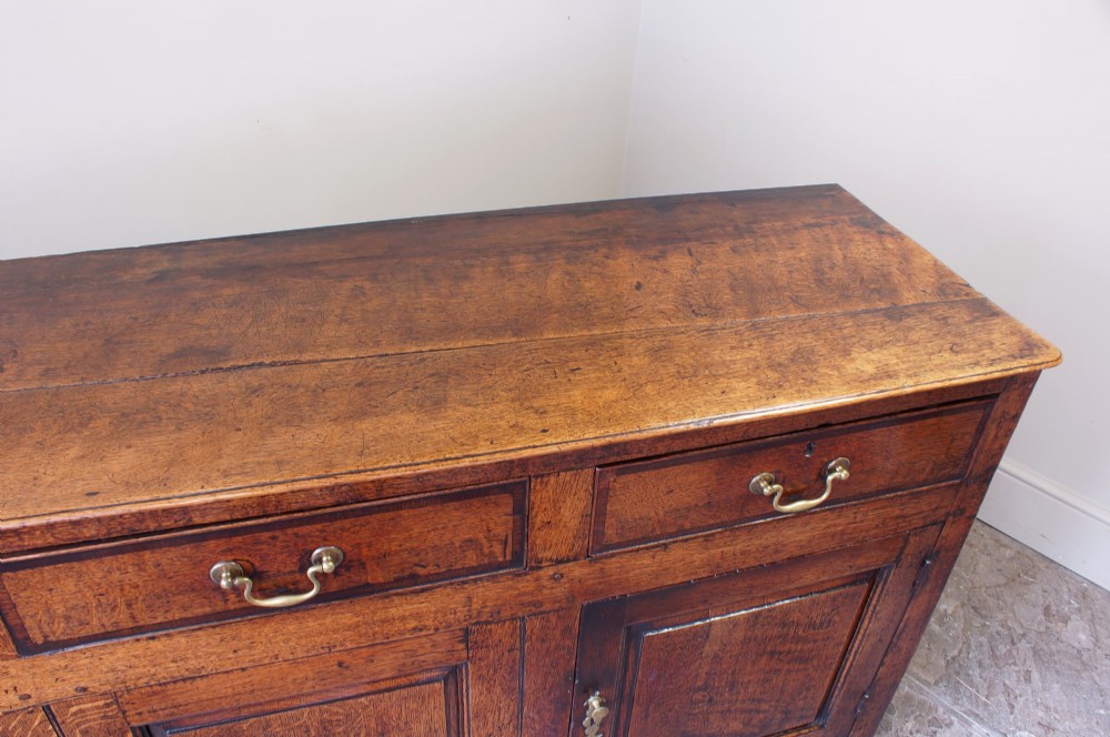A Georgian oak dresser base featuring three top drawers with brass handles above three panelled cupboard doors. View IX