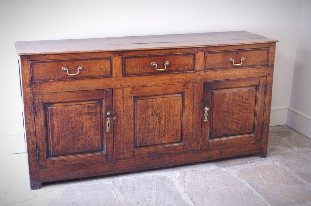 A Georgian oak dresser base featuring three top drawers with brass handles above three panelled cupboard doors.