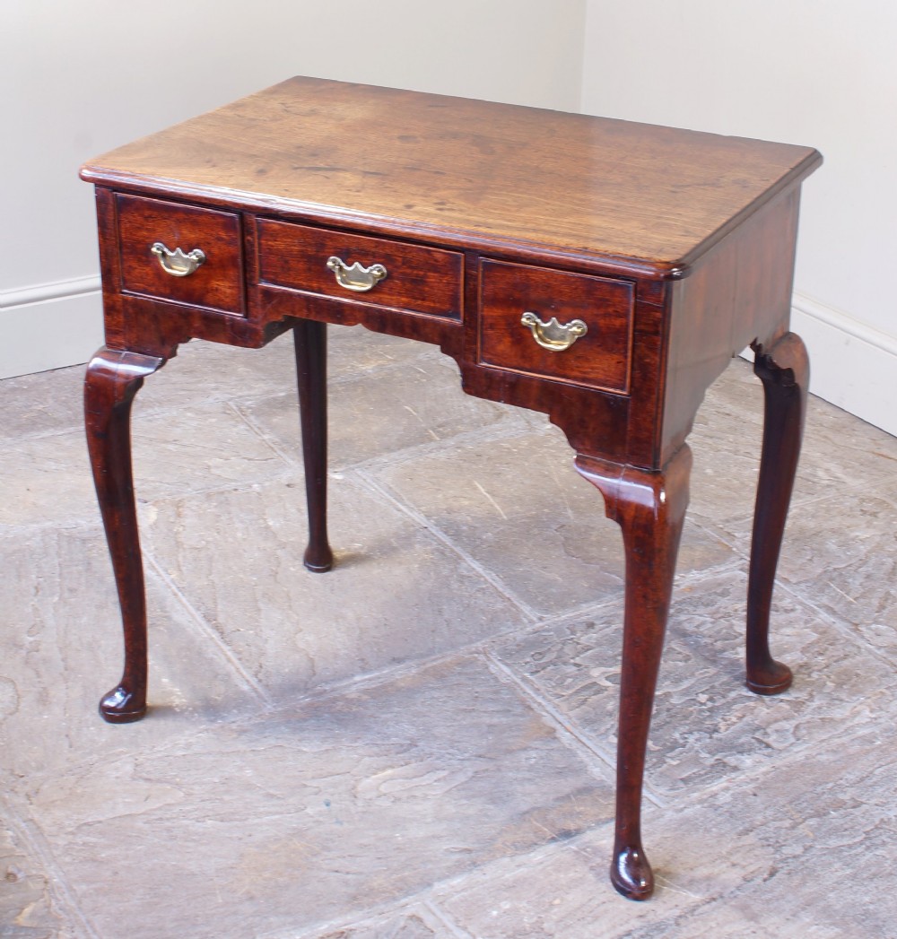 A mid-18th century George II mahogany lowboy featuring three drawers with brass handles, a shaped apron, and four cabriole legs ending in pad feet.