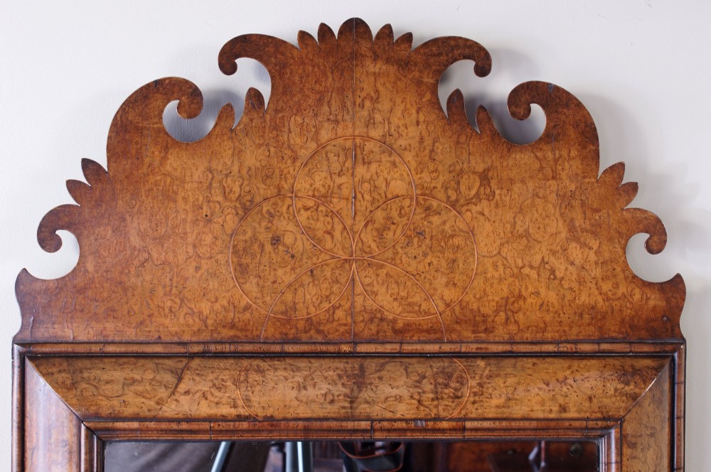 A rectangular William and Mary style wall mirror framed in burr walnut veneer with a cushion moulding and an intricately shaped fretwork crest. View IX