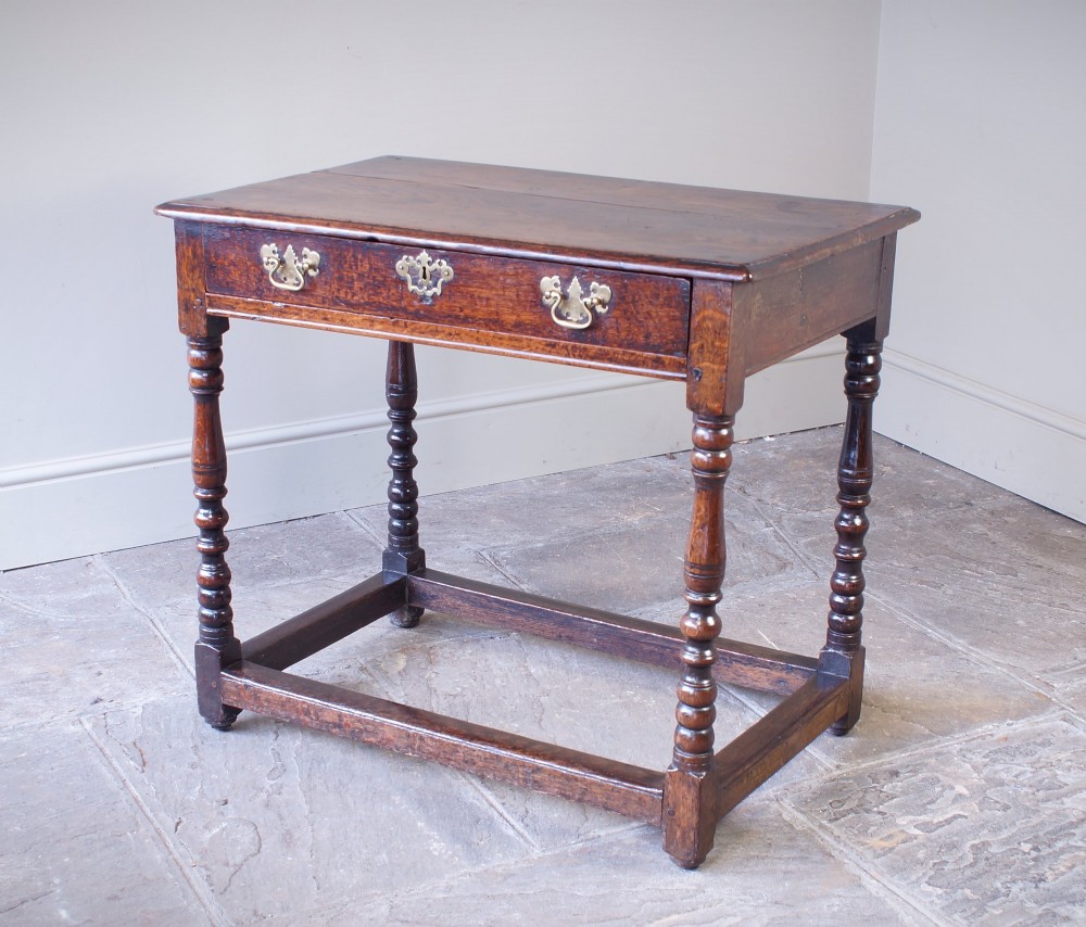 A late 17th-century dark oak side table featuring a single drawer with brass handles, turned legs, and a rectangular stretcher base. View II
