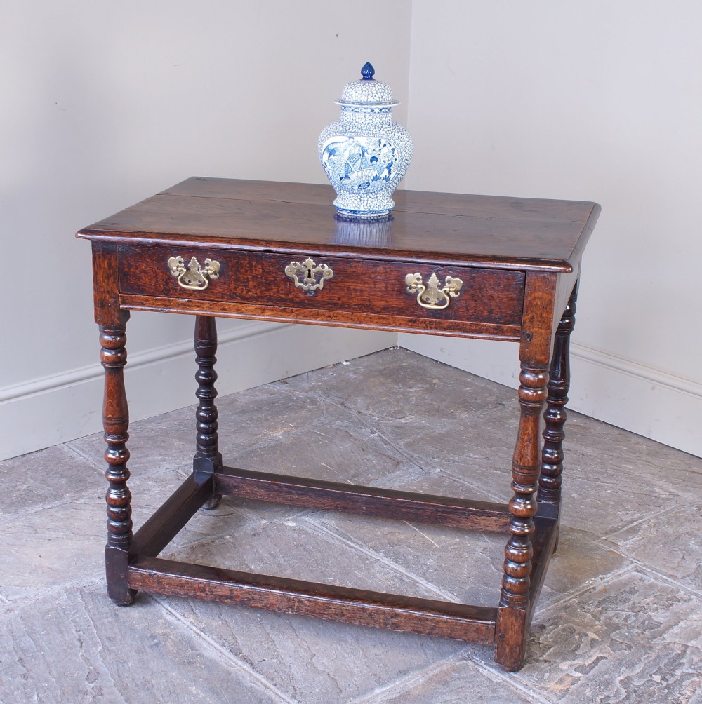 A late 17th-century dark oak side table featuring a single drawer with brass handles, turned legs, and a rectangular stretcher base. View V