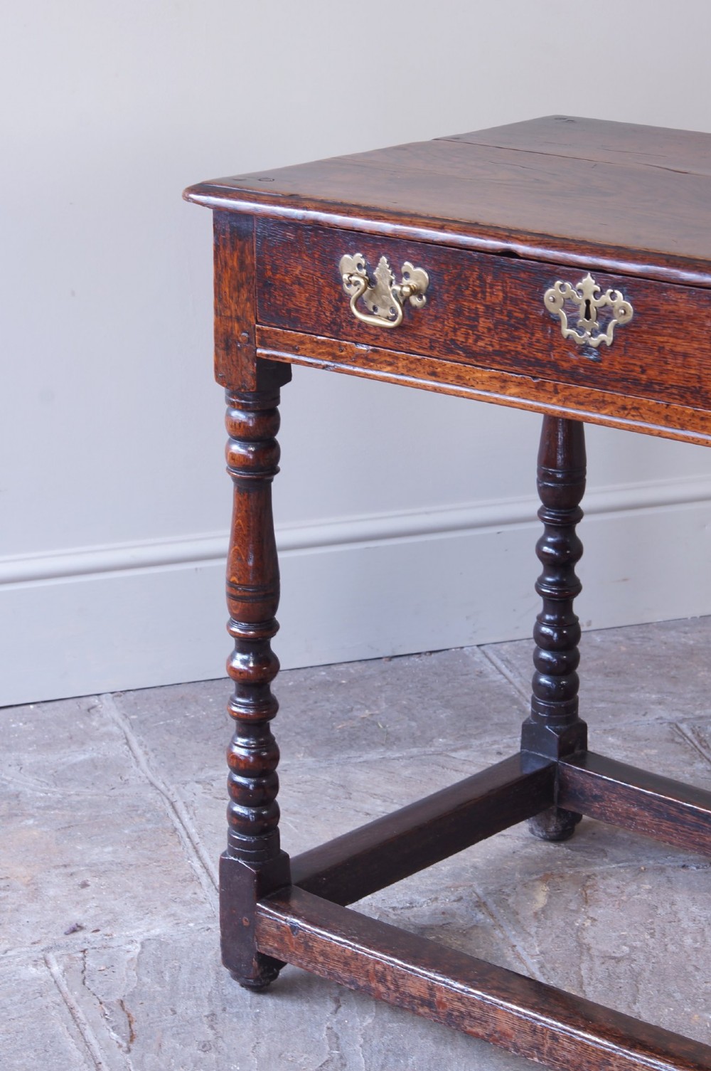 A late 17th-century dark oak side table featuring a single drawer with brass handles, turned legs, and a rectangular stretcher base. View VI