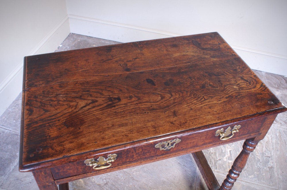 A late 17th-century dark oak side table featuring a single drawer with brass handles, turned legs, and a rectangular stretcher base. View X