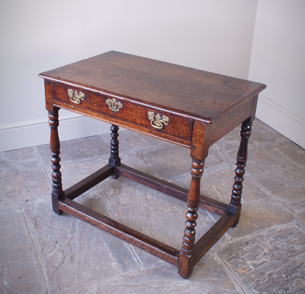 A late 17th-century dark oak side table featuring a single drawer with brass handles, turned legs, and a rectangular stretcher base.