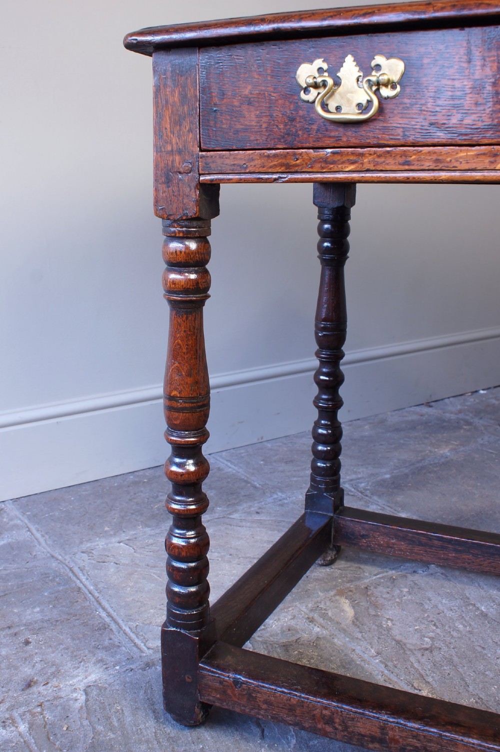 A late 17th-century dark oak side table featuring a single drawer with brass handles, turned legs, and a rectangular stretcher base. View XI