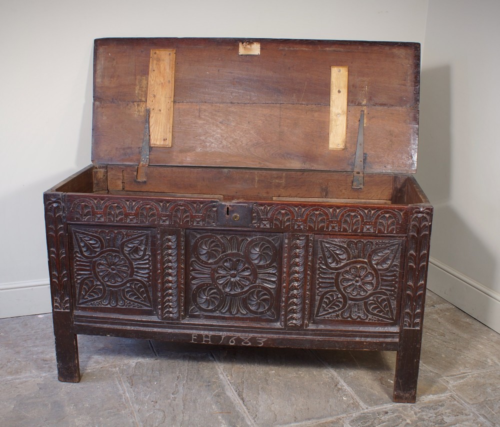 A 17th-century dark oak coffer with three carved floral panels, an iron lock plate, and a dated inscription reading FH 1683 along the front rail. View IV
