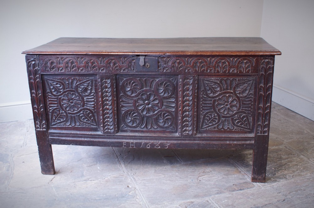 A 17th-century dark oak coffer with three carved floral panels, an iron lock plate, and a dated inscription reading FH 1683 along the front rail.