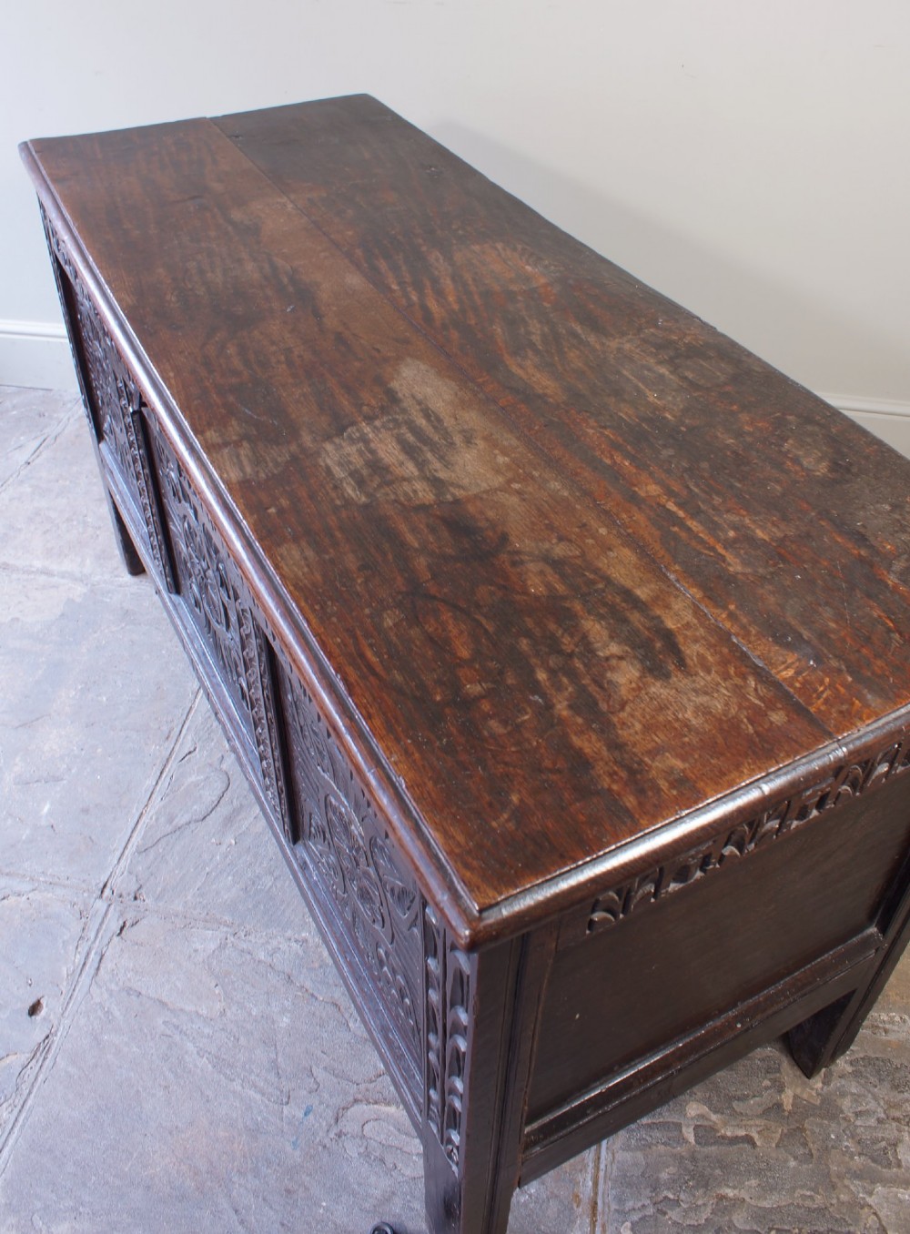 A 17th-century dark oak coffer with three carved floral panels, an iron lock plate, and a dated inscription reading FH 1683 along the front rail. View V