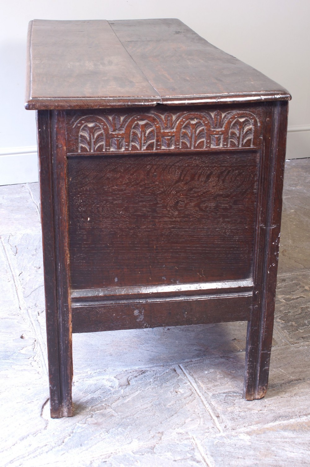A 17th-century dark oak coffer with three carved floral panels, an iron lock plate, and a dated inscription reading FH 1683 along the front rail. View VI