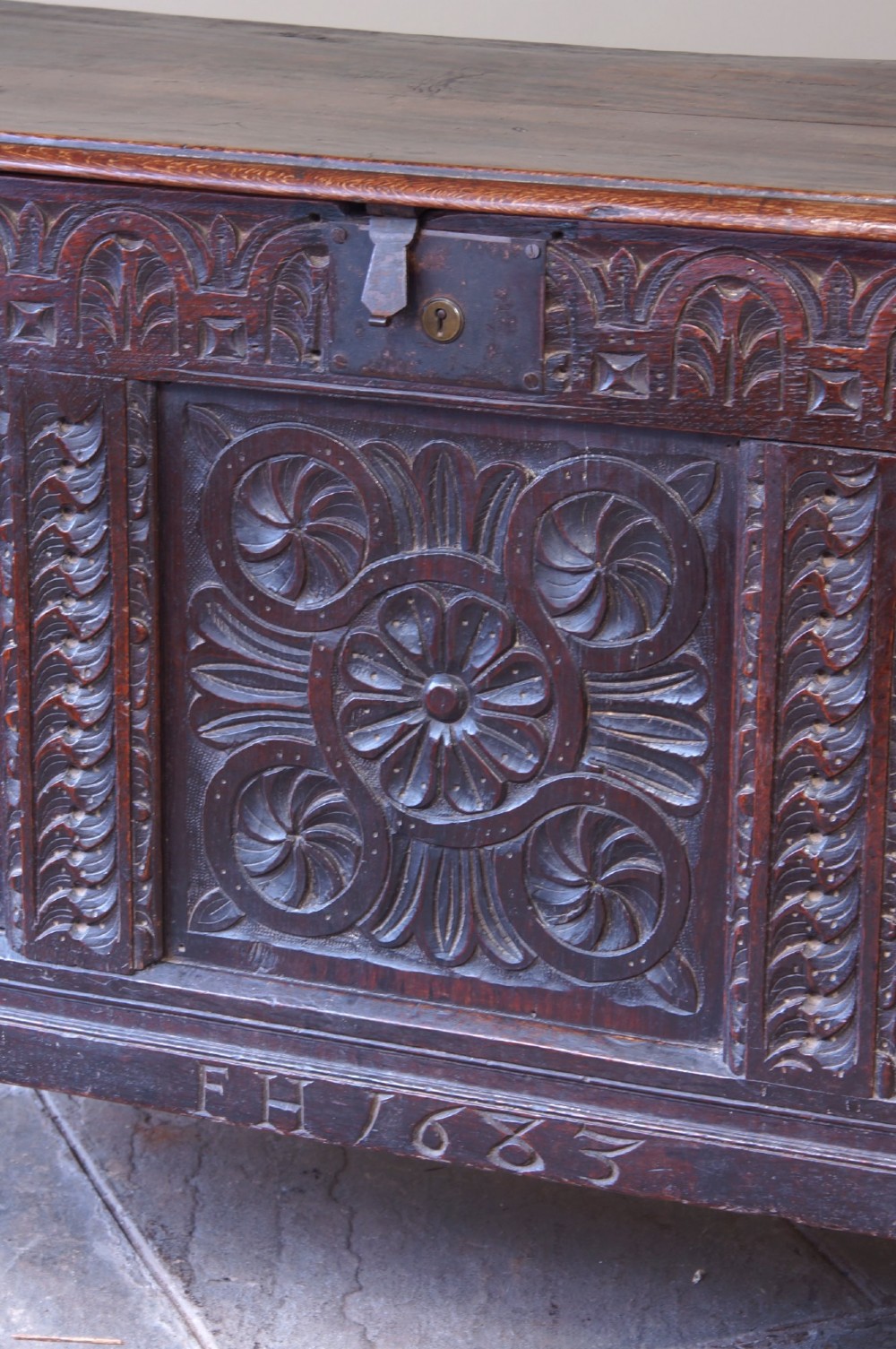A 17th-century dark oak coffer with three carved floral panels, an iron lock plate, and a dated inscription reading FH 1683 along the front rail. View IX
