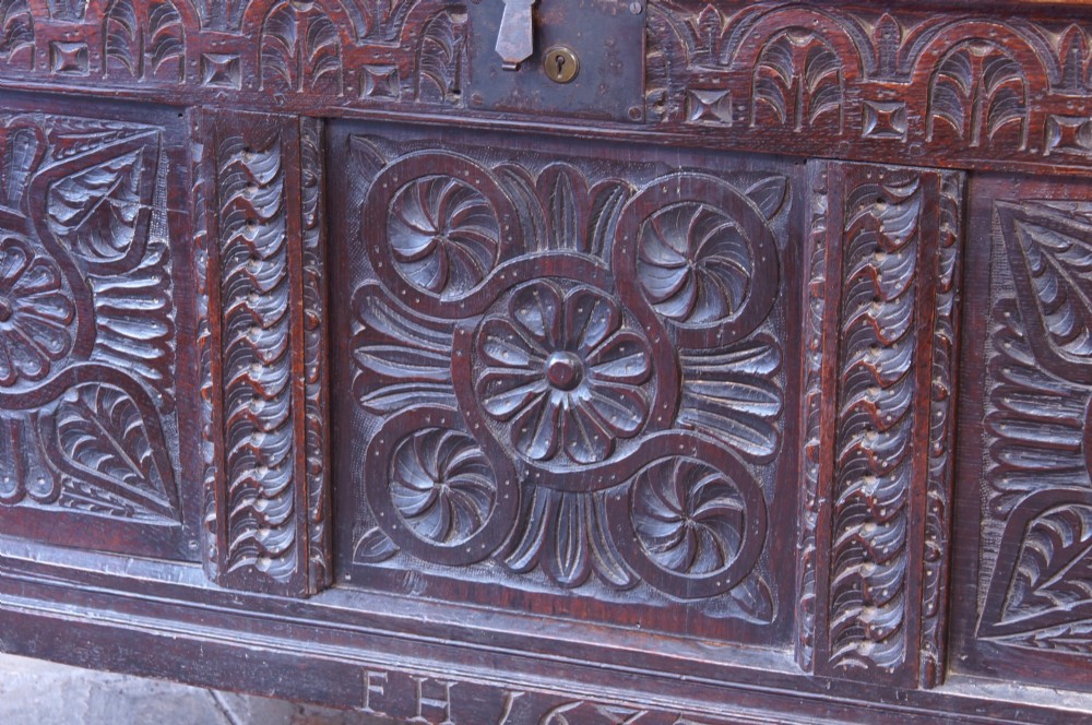 A 17th-century dark oak coffer with three carved floral panels, an iron lock plate, and a dated inscription reading FH 1683 along the front rail. View X