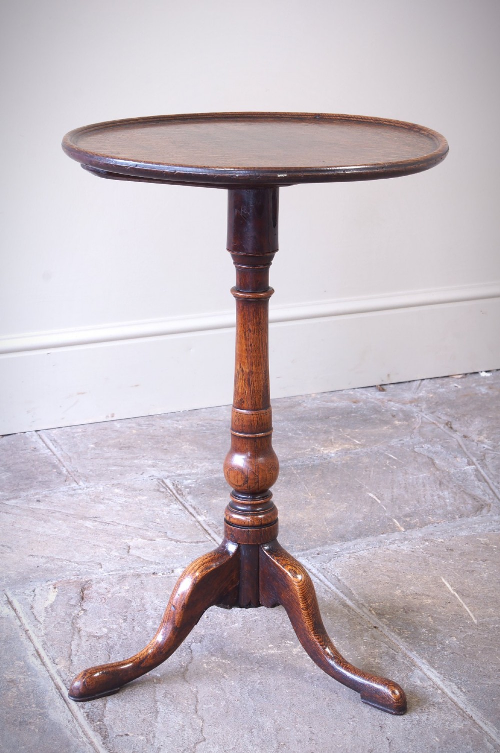 An 18th-century dark oak tripod table featuring a circular top, turned central baluster stem, and three splayed legs.