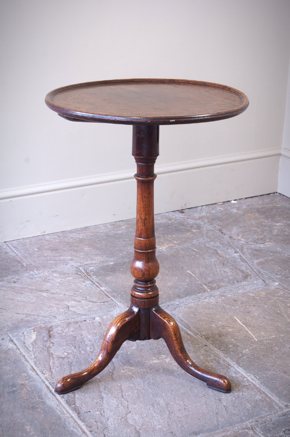 An 18th-century dark oak tripod table featuring a circular top, turned central baluster stem, and three splayed legs. View VII