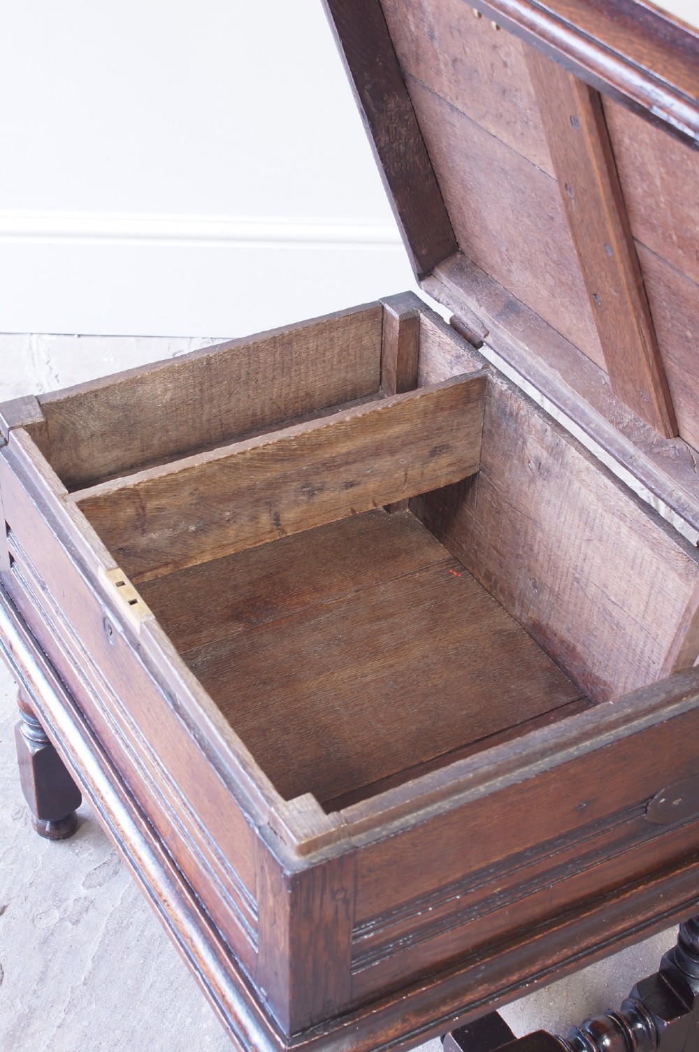 A 17th-century dark oak box stool with a flat hinged top, moulded panel front, and turned legs joined by a bobbin stretcher. View VI