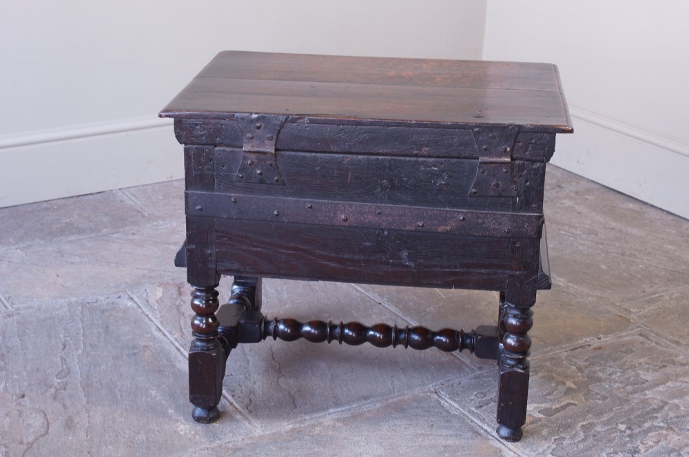 A 17th-century dark oak box stool with a flat hinged top, moulded panel front, and turned legs joined by a bobbin stretcher. View VIII
