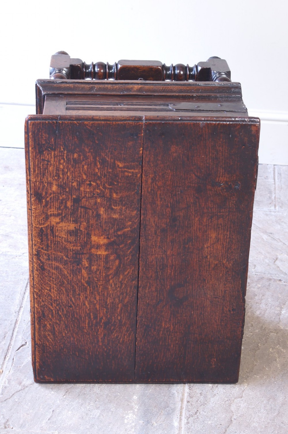 A 17th-century dark oak box stool with a flat hinged top, moulded panel front, and turned legs joined by a bobbin stretcher. View IX