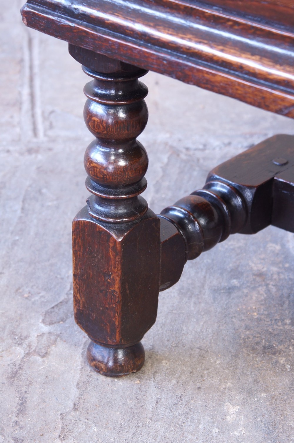 A 17th-century dark oak box stool with a flat hinged top, moulded panel front, and turned legs joined by a bobbin stretcher. View XI