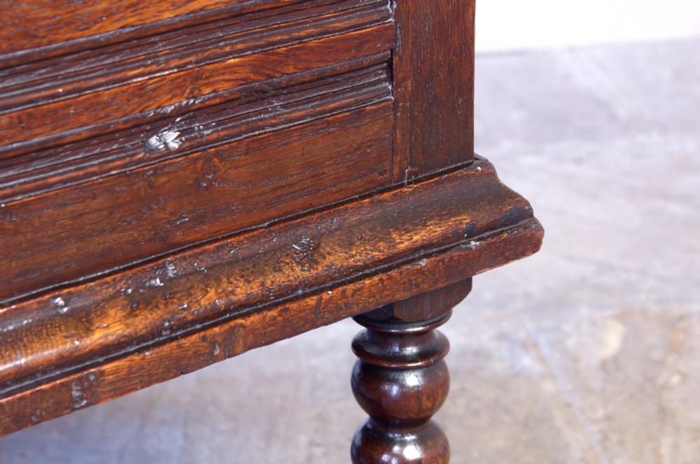 A 17th-century dark oak box stool with a flat hinged top, moulded panel front, and turned legs joined by a bobbin stretcher. View XII