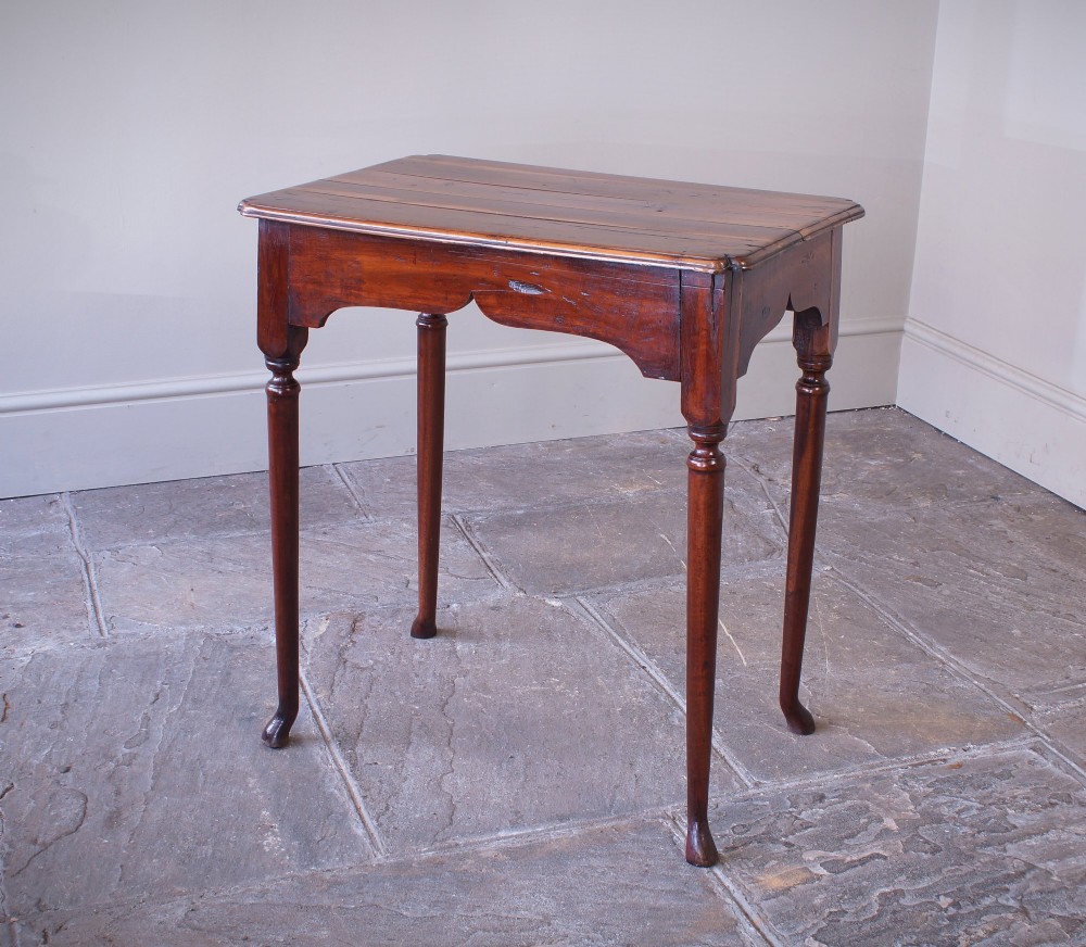 An early 18th-century fruitwood centre table featuring a rectangular plank top, a scalloped apron, and slender turned legs ending in pad feet.