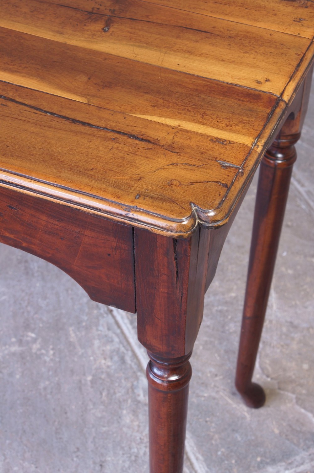 An early 18th-century fruitwood centre table featuring a rectangular plank top, a scalloped apron, and slender turned legs ending in pad feet. View IX