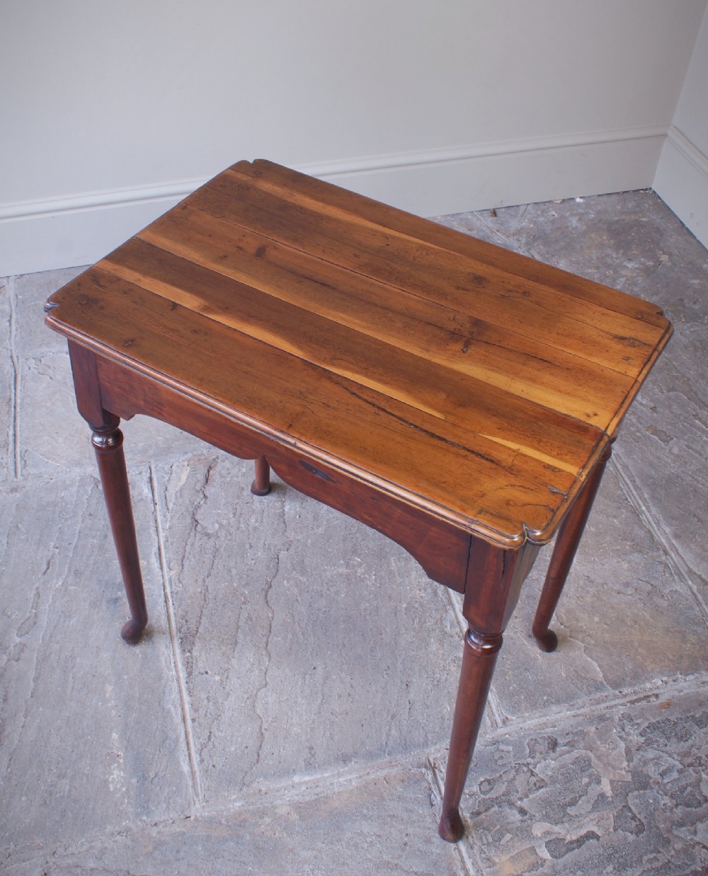 An early 18th-century fruitwood centre table featuring a rectangular plank top, a scalloped apron, and slender turned legs ending in pad feet. View X
