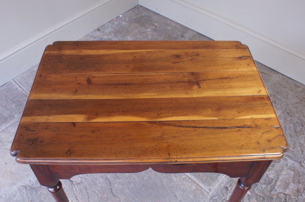 An early 18th-century fruitwood centre table featuring a rectangular plank top, a scalloped apron, and slender turned legs ending in pad feet. View XII