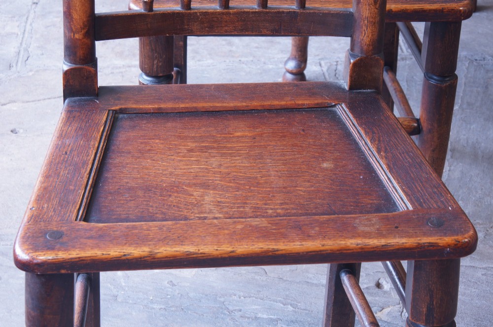 A set of six dark oak country dining chairs featuring carved shell crest rails, spindle backs, turned legs, and solid wood panel seats. View II