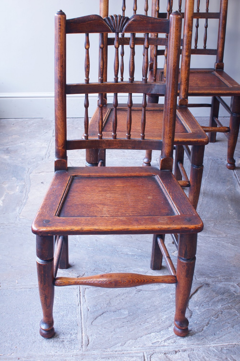 A set of six dark oak country dining chairs featuring carved shell crest rails, spindle backs, turned legs, and solid wood panel seats. View III