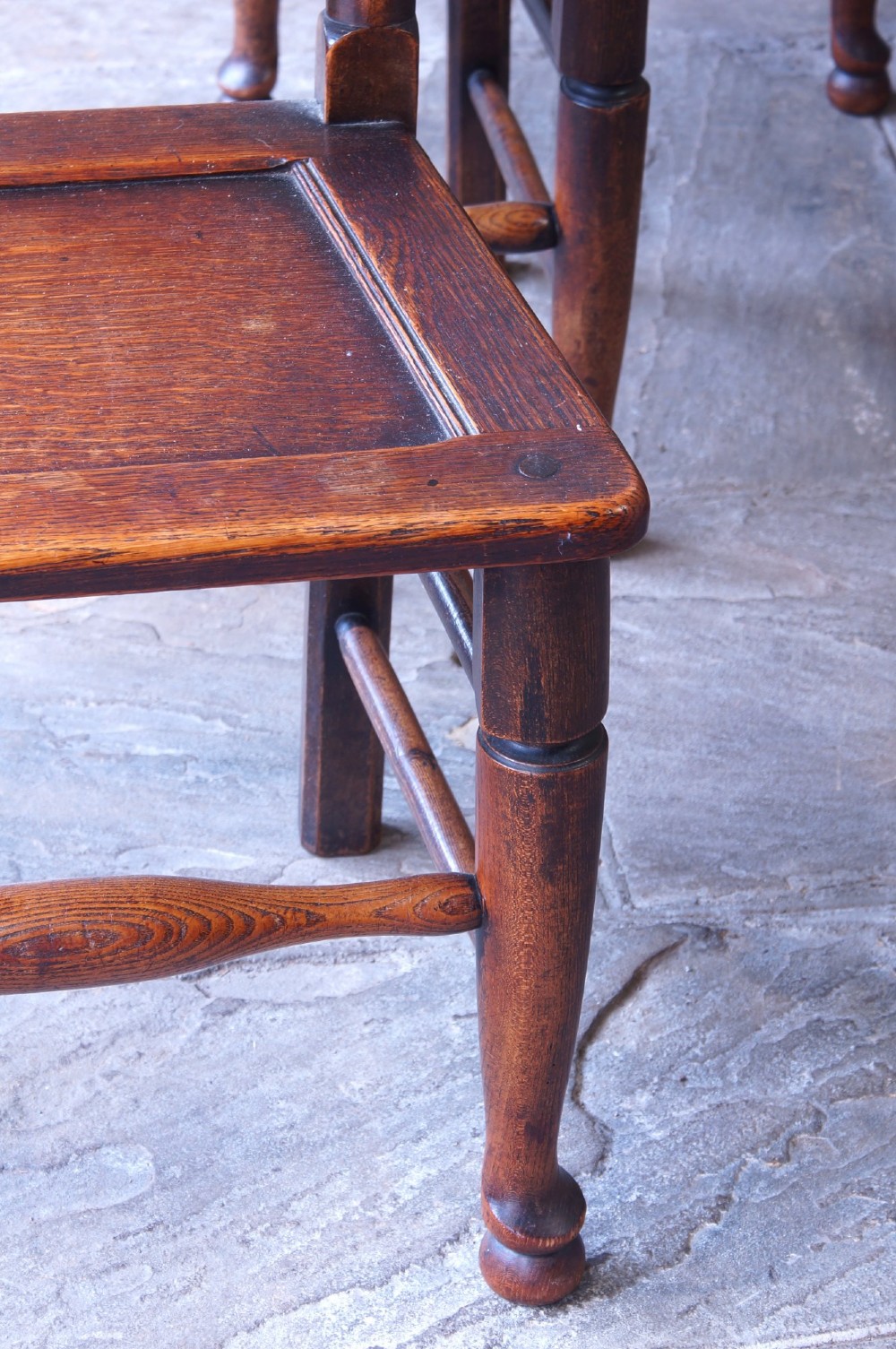 A set of six dark oak country dining chairs featuring carved shell crest rails, spindle backs, turned legs, and solid wood panel seats. View IV