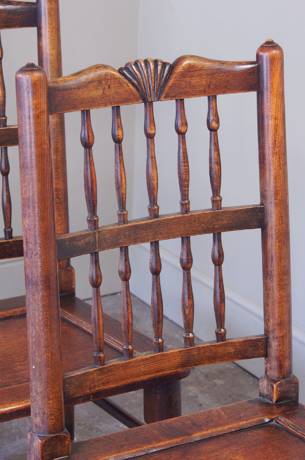 A set of six dark oak country dining chairs featuring carved shell crest rails, spindle backs, turned legs, and solid wood panel seats. View V